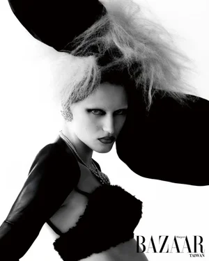 Monochrome fashion portrait of a woman wearing an oversized black sculptural hat and textured top against a white backdrop.