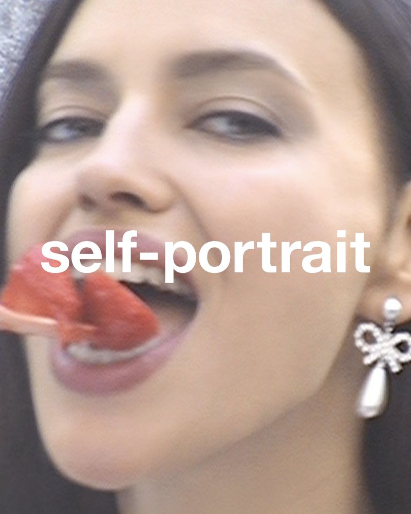 Close-up of a brunette adult woman eating a red strawberry. She is wearing a silver, bow-shaped earring with a pearl drop.