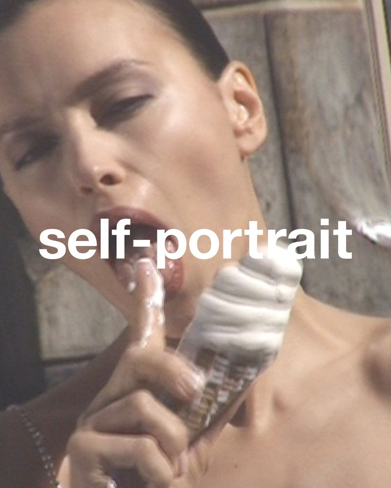 Close-up of a light-skinned adult female holding an ice cream cone and licking melted ice cream off her finger in soft daylight.