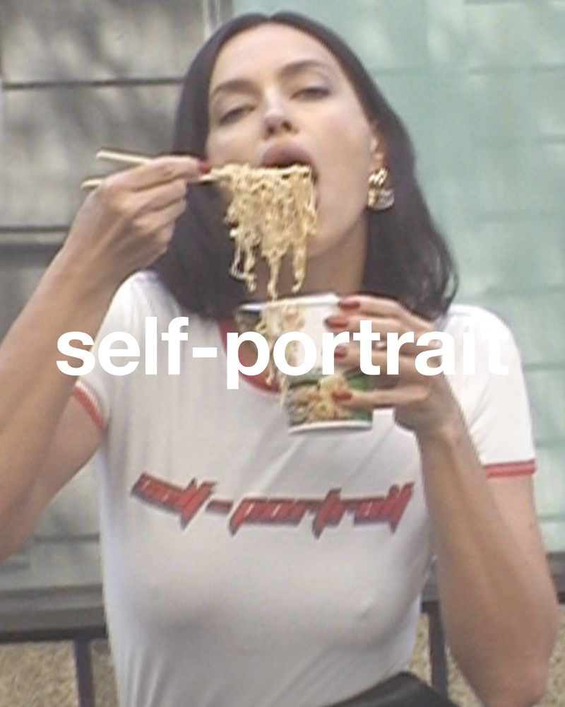 Adult woman eats noodles with chopsticks in an outdoor setting, wearing a white t-shirt.  Close up shows off black hair and dangling earrings.