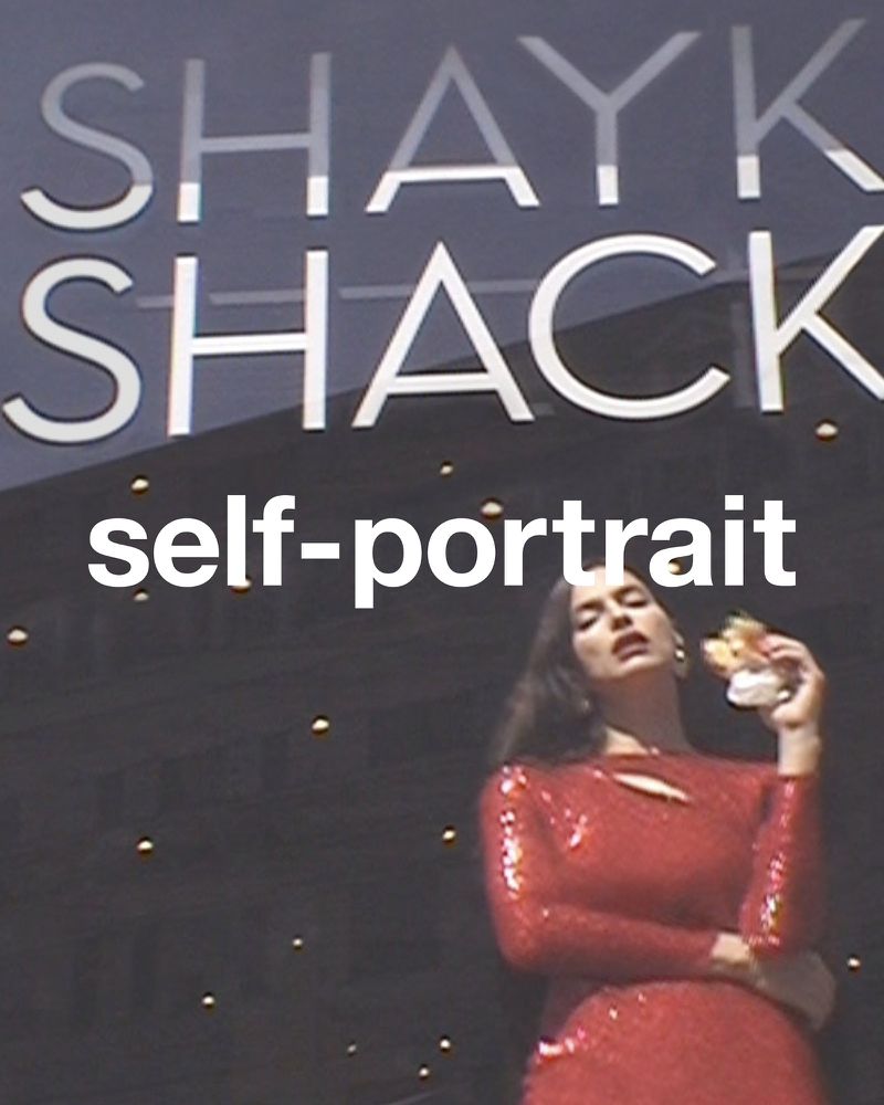 Adult female in a red sequined dress poses with an object near a building with “SHAYK SHACK” signage; indoors, medium shot.