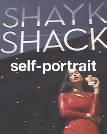 Adult female in a red sequined dress poses with an object near a building with “SHAYK SHACK” signage; indoors, medium shot.