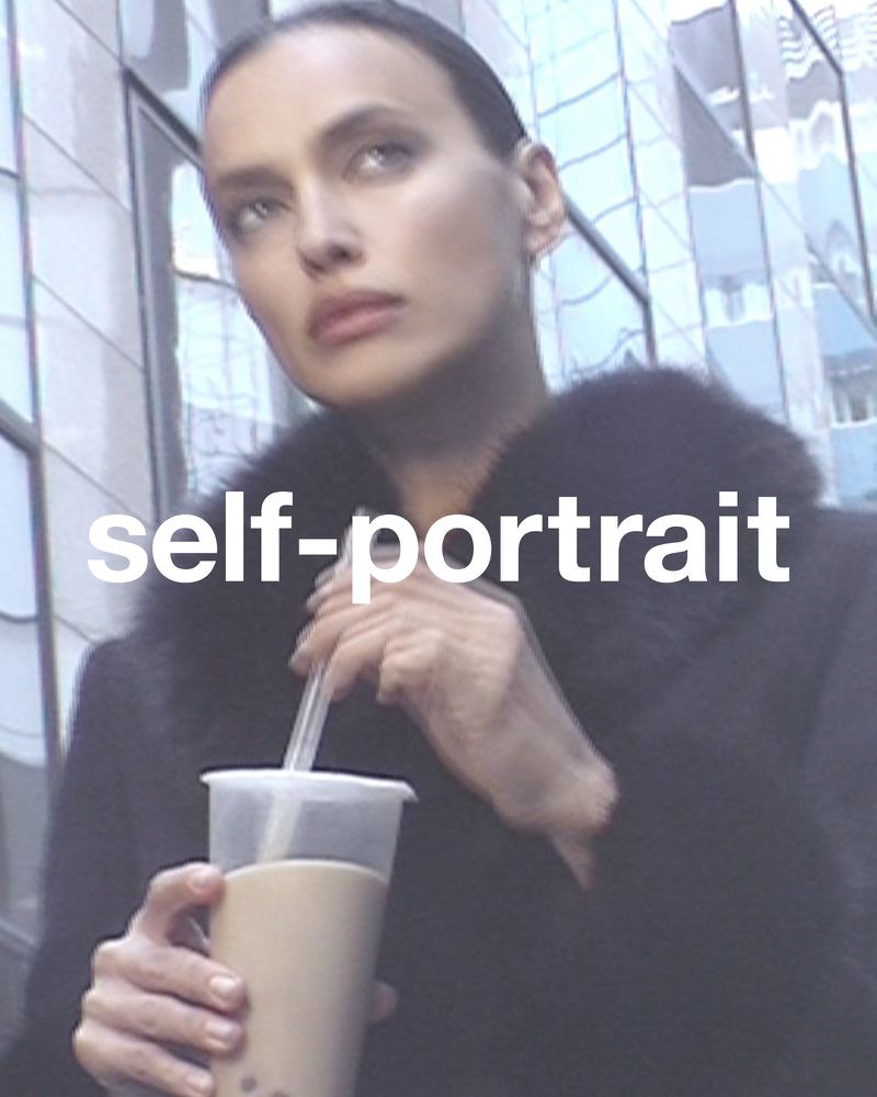 Close-up of a woman in a black coat drinking boba tea outdoors against a building with reflective glass windows during the daytime.