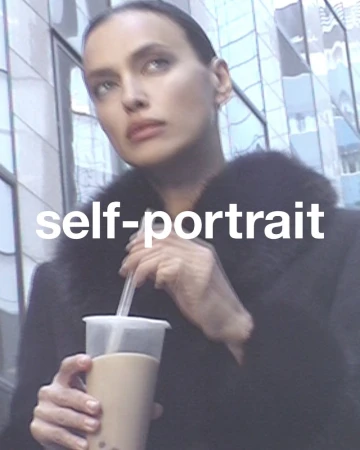 Close-up of a woman in a black coat drinking boba tea outdoors against a building with reflective glass windows during the daytime.