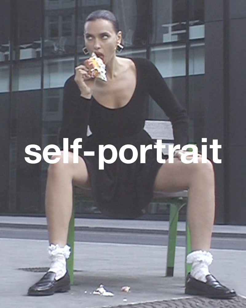 Adult woman in a black dress eating pastry while sitting on a bench in front of a building with many windows, wearing ruffle socks.