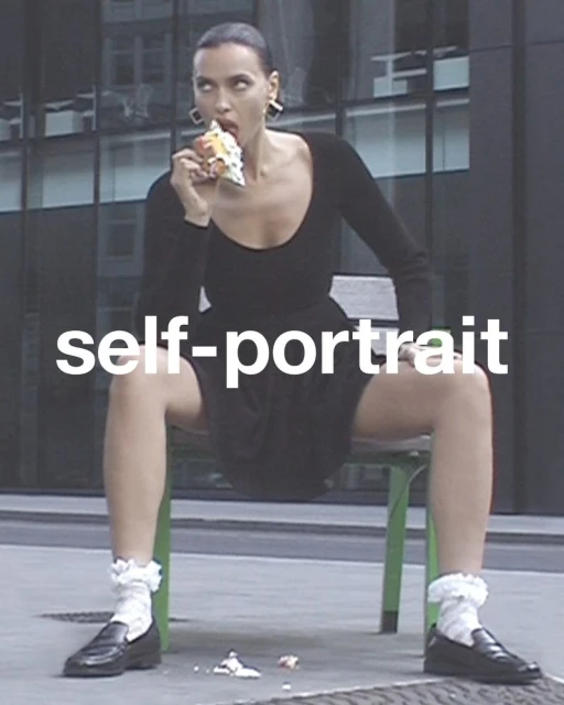 Adult woman in a black dress eating pastry while sitting on a bench in front of a building with many windows, wearing ruffle socks.