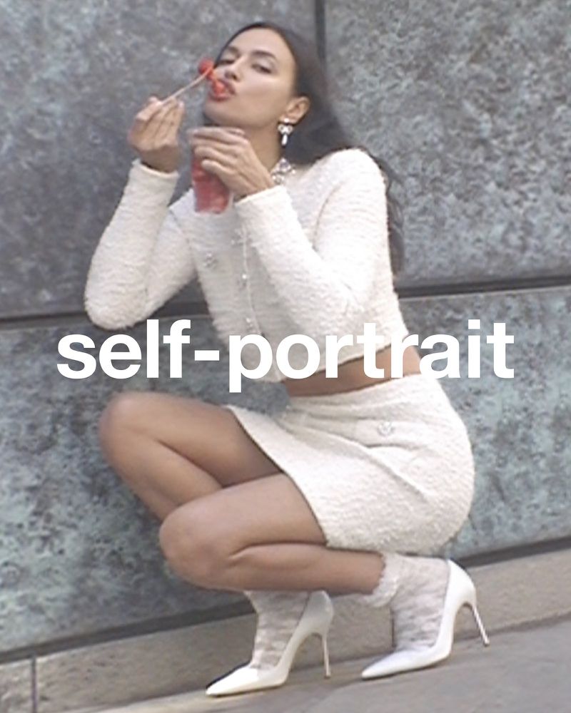 Attractive woman in stylish cream-colored two-piece set squats in a fashionable pose while eating red berries from a clear beverage container.