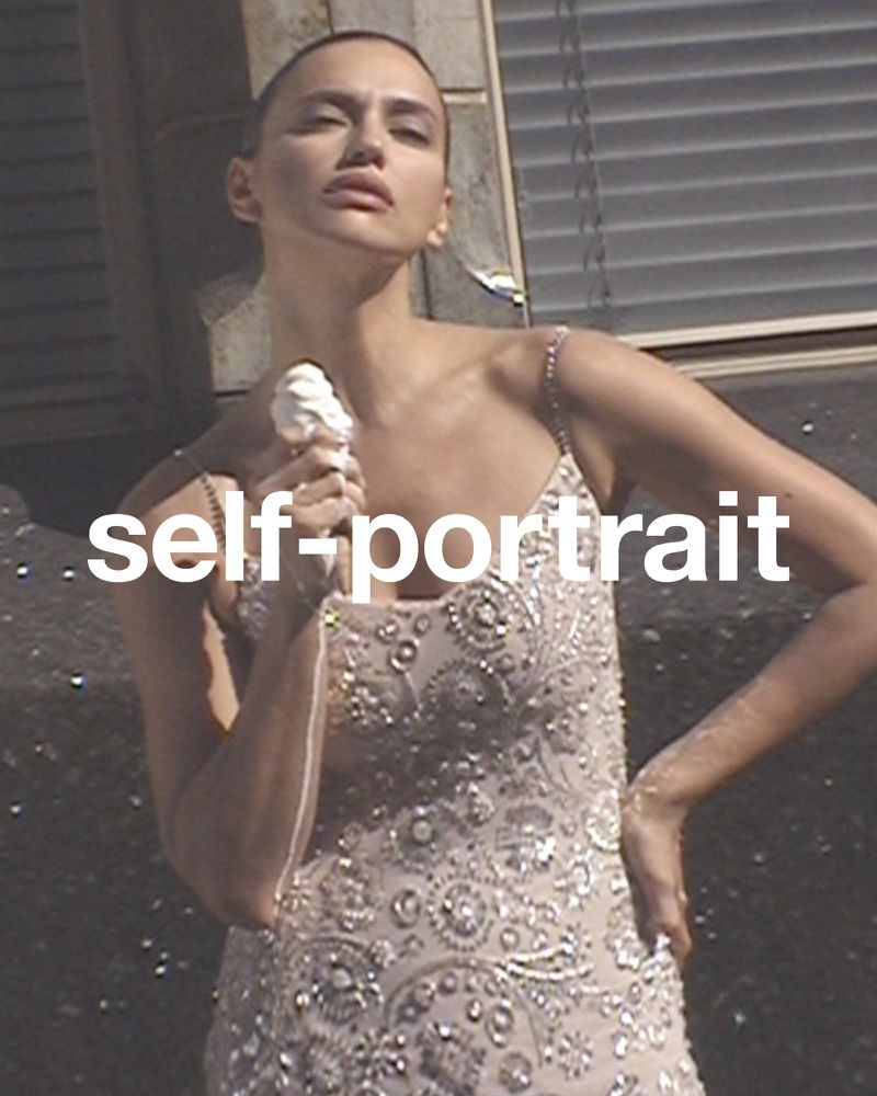 Glamorous portrait of a fair-skinned adult woman in an embellished dress, holding a white object, set against an exterior background.