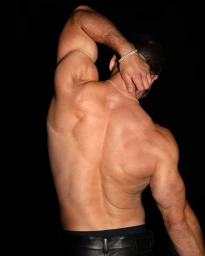 Muscular man with back turned posing with hand behind head against a black background