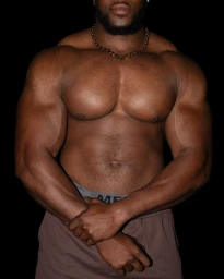 Close-up portrait of a muscular man wearing a chain necklace against a dark background for Fantastic Man.