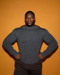 Muscular black man wearing a grey textured sweater against a solid gold background for Fantastic Man.