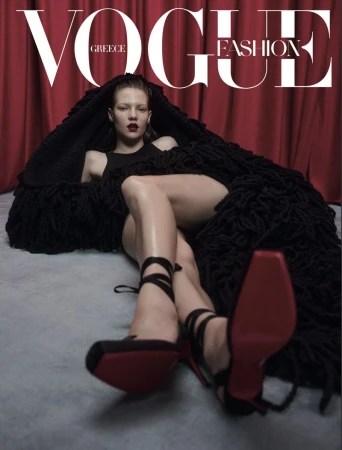 Vogue Greece fashion magazine cover featuring a fashion model in black shoes and a black outfit with a red backdrop.