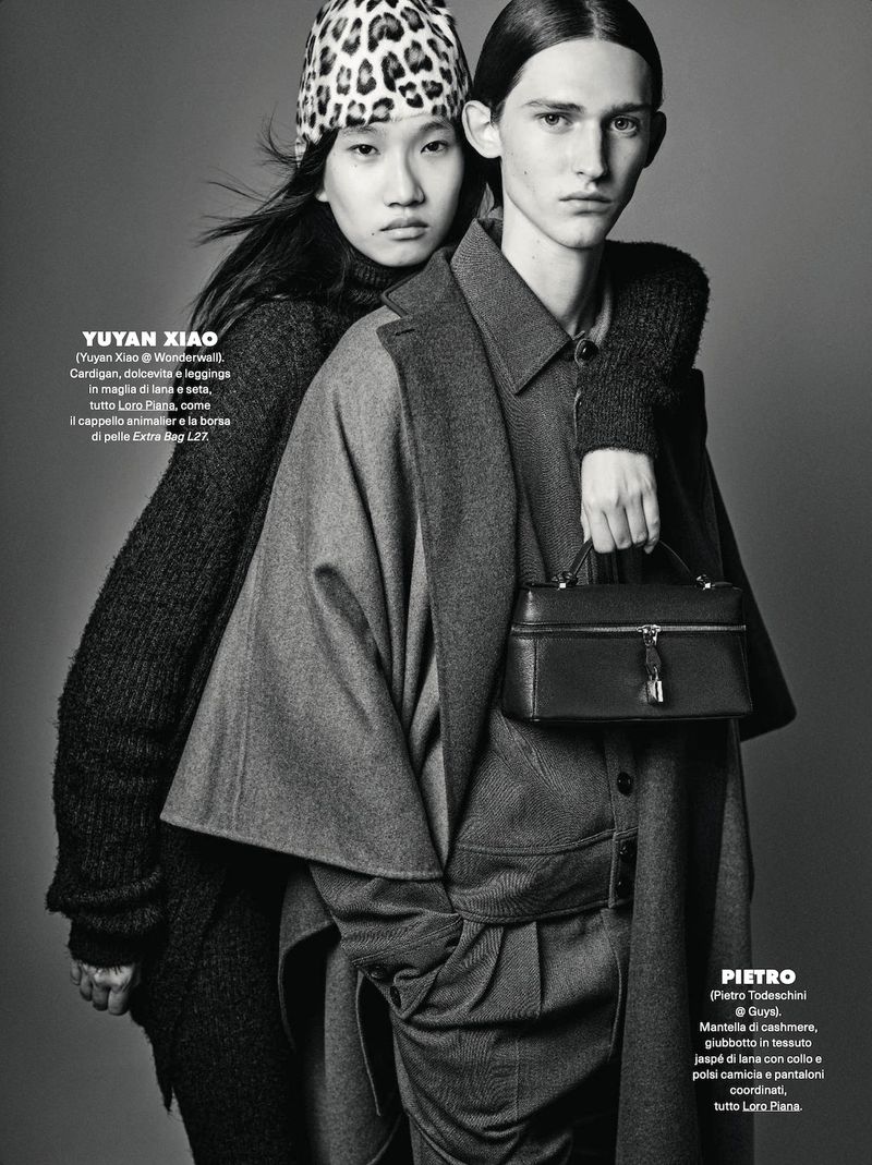 Two fashion models pose in a black and white studio shot. One model wears a leopard print hat, while the other carries a structured box bag.