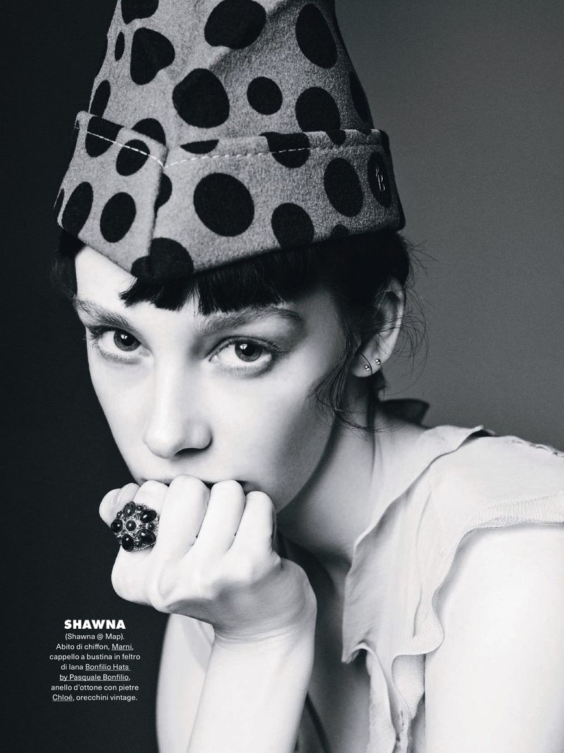 Black and white portrait of a young woman with short bangs and a polka dot hat. She is wearing a large ring and a light coloured dress.