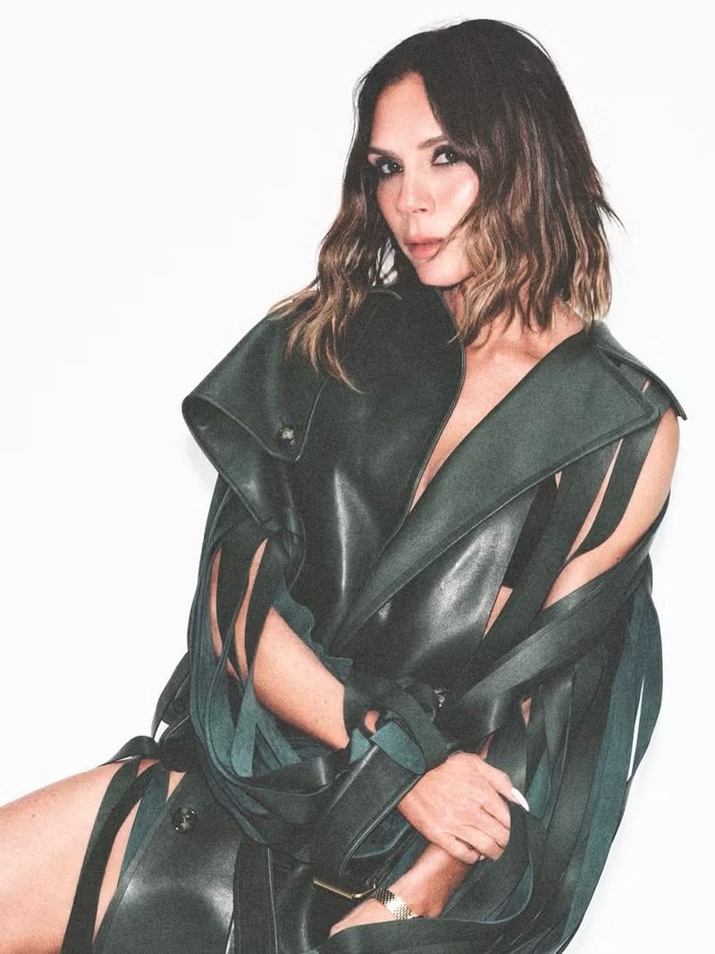 Brunette woman in an unusual leather jacket posing against a bright white background in a studio setting for a fashion editorial shoot.