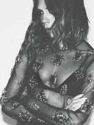 Victoria Beckham wearing a jewelled sheer black top with arms crossed against a plain white background