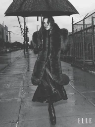 Victoria Beckham holding an umbrella while walking down a wet city street in a fur coat and platform boots for an Elle U.S. editorial shoot.