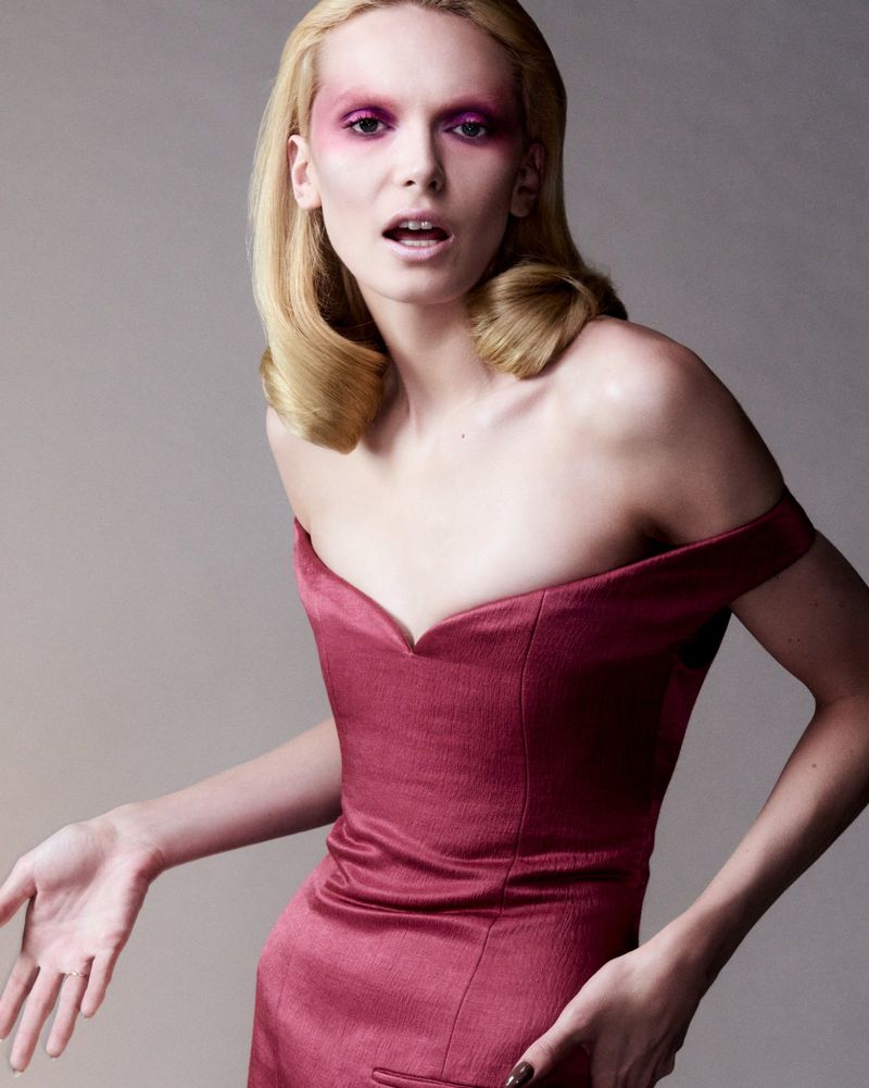 Woman in red dress with pink eye makeup poses in a photo studio. Shoulder-length blonde hair, light skin tone, dramatic makeup.