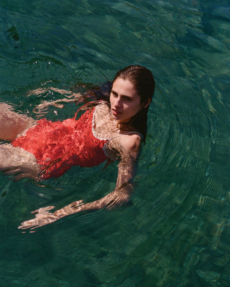 Woman in red swimsuit swimming in clear blue water. View from above. Ripples on the surface. Summer vacation.