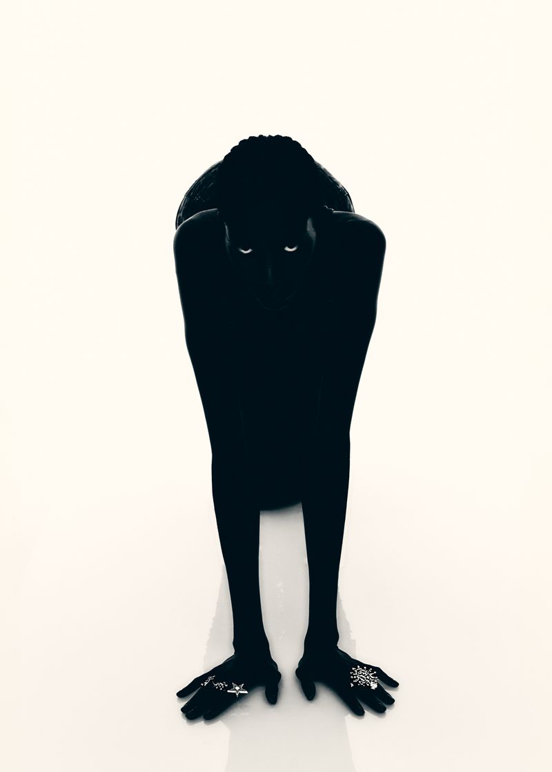 Striking studio shot of a Black model posing in shadow against bright white, rings on hands, creating a stark contrast and artful silhouette.