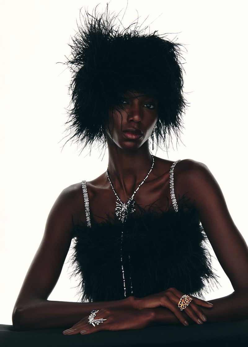 Portrait of a dark-skinned woman wearing a feathered hat and jewelry in a studio setting against a white background. Fashion editorial.