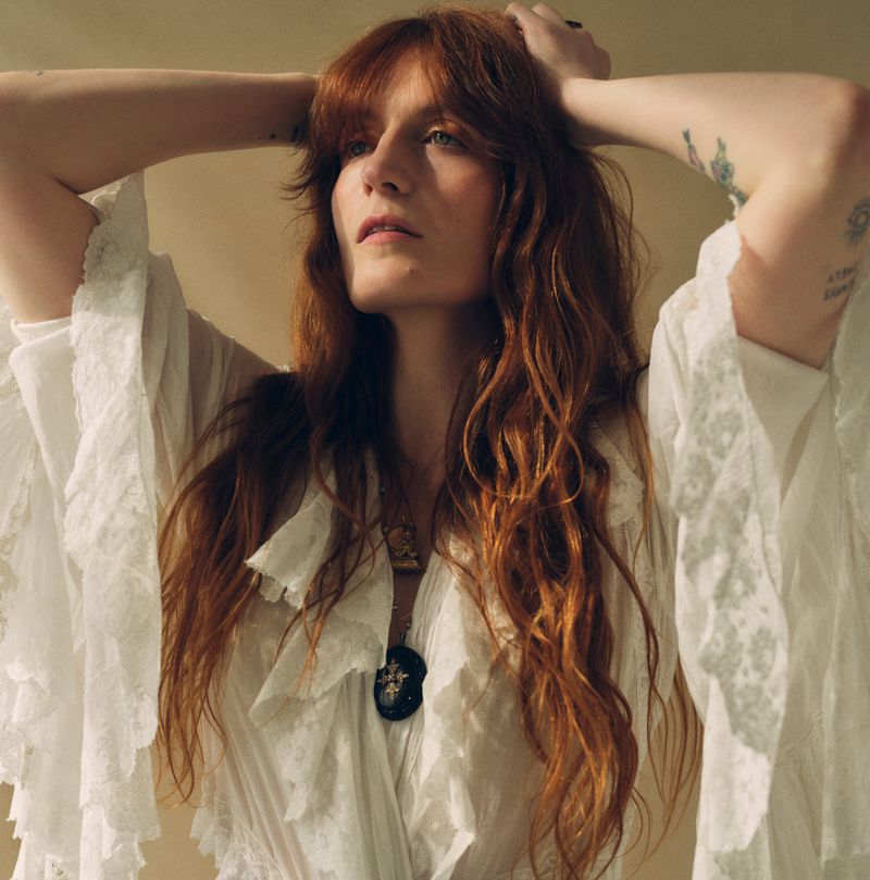 Close-up of a red-haired woman in a white lace dress with her hands behind her head looking up in a photo studio setting.