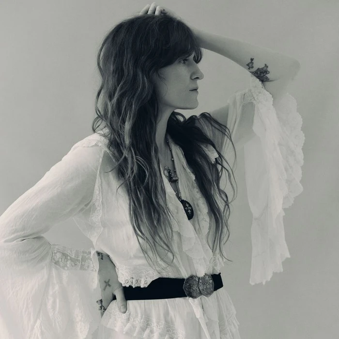 Florence Welch wearing a white ruffled blouse with wide sleeves against a plain background