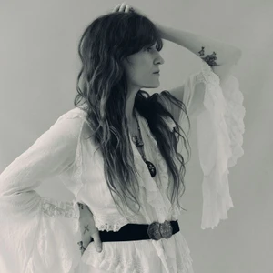 Florence Welch wearing a white ruffled blouse with wide sleeves against a plain background