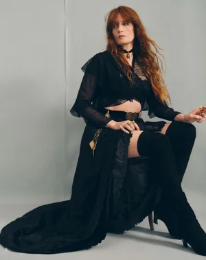Florence Welch seated in a black outfit with thigh-high boots against a grey studio backdrop for The Guardian.
