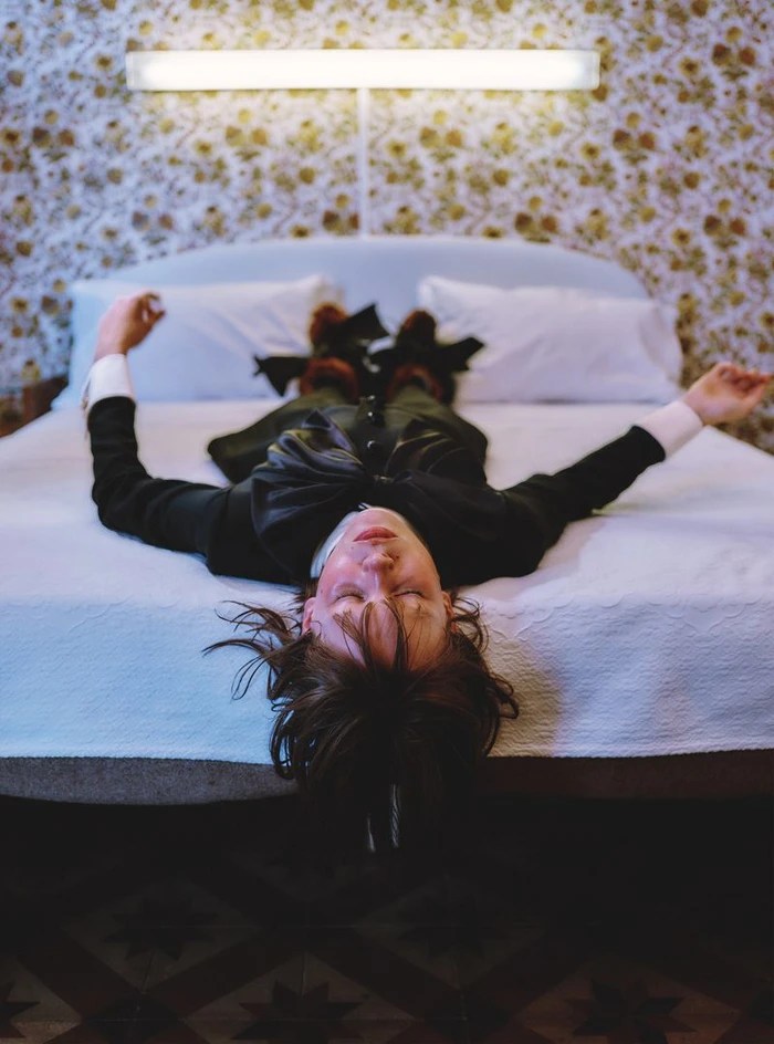 Model lying upside down on a white bed in a patterned room for Vogue Italia