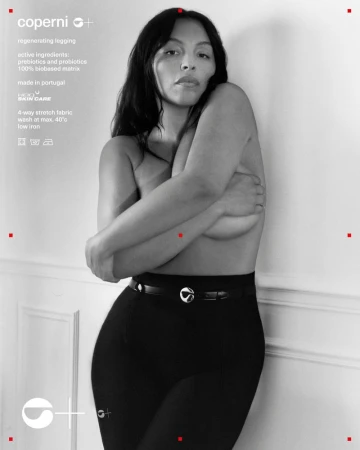 Adult woman in black leggings poses against a light wall, arms crossed covering her chest, in a studio shot with soft lighting.