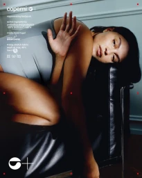 Model Paloma Elsesser reclining in a grey Coperni bodysuit over a black leather chair in an interior setting.
