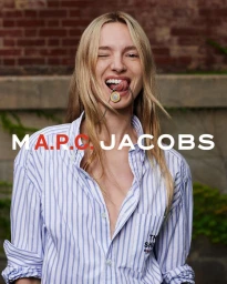 Model wearing a blue and white striped shirt holding a pendant in her mouth against a brick exterior