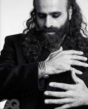 Black and white portrait of a bearded man with long hair wearing a black jacket and a silver cuff bracelet.
