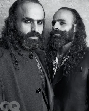 Black and white portrait of the Nasser brothers with long dark hair, full beards, and heavy eyeliner wearing dark coats.