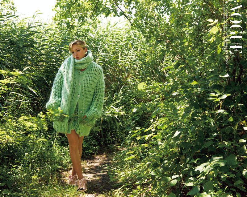 Fashion editorial: A woman in a green knit outfit poses in a lush green outdoor environment for a Vogue magazine fashion shoot.