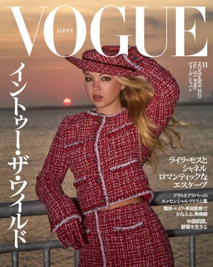 Model Lila Moss wearing a red tweed jacket and matching hat against a sunset water backdrop for Vogue Japan