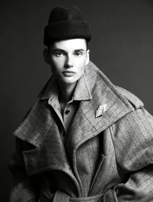 Model Giedre Dukauskaite wearing a structured grey coat and dark hat in a black and white editorial portrait by Javier Biosca.