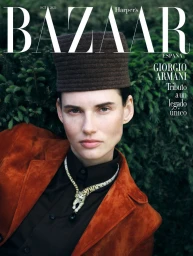 Model Giedre Dukauskaite wearing brown pillbox hat and rust suede jacket against dense green foliage background.