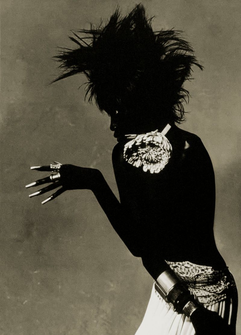 Artistic black and white portrait of a woman with dramatic hair and unique jewelry posing in a studio with soft lighting.