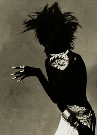 Artistic black and white portrait of a woman with dramatic hair and unique jewelry posing in a studio with soft lighting.