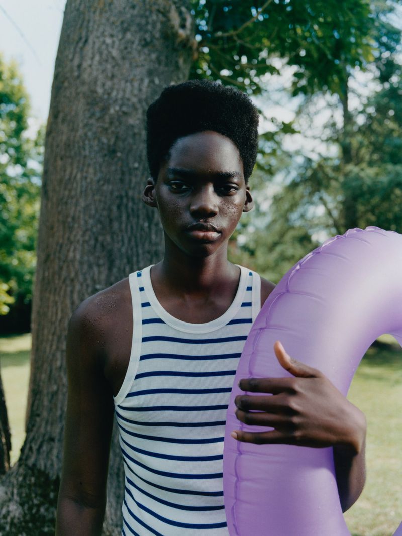 Portrait of African woman wearing a striped tank top and holding a purple inflatable ring in front of a tree in natural lighting.