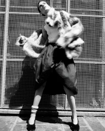 Model Libby Taverner wearing a fluffy patterned jacket and dark skirt posed against a metal grid wall for Pop Magazine.