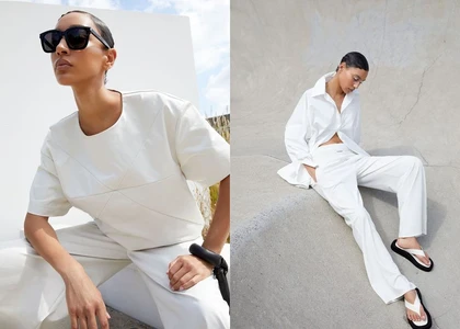 A woman wearing a white short-sleeve top and sunglasses poses against a white and concrete background.