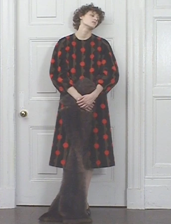 Adult female model wearing a brown dress with red polka dots posing in front of a white door inside a room with white walls.