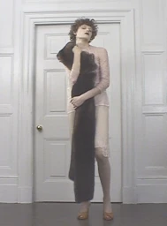 Model standing in front of a white panelled door holding a long dark fur stole for an AnOther Magazine editorial by Sharna Osborne