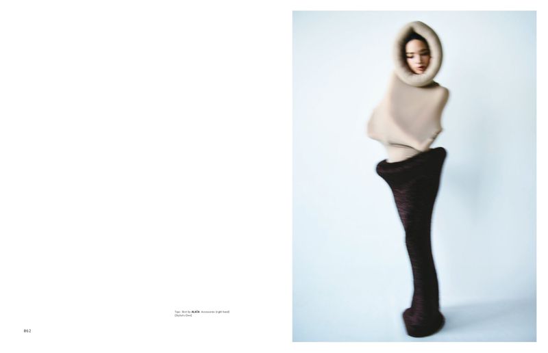 Fashion shot of a woman in an unusual tan and brown sculpted garment against a light blue background, modern and avant-garde.