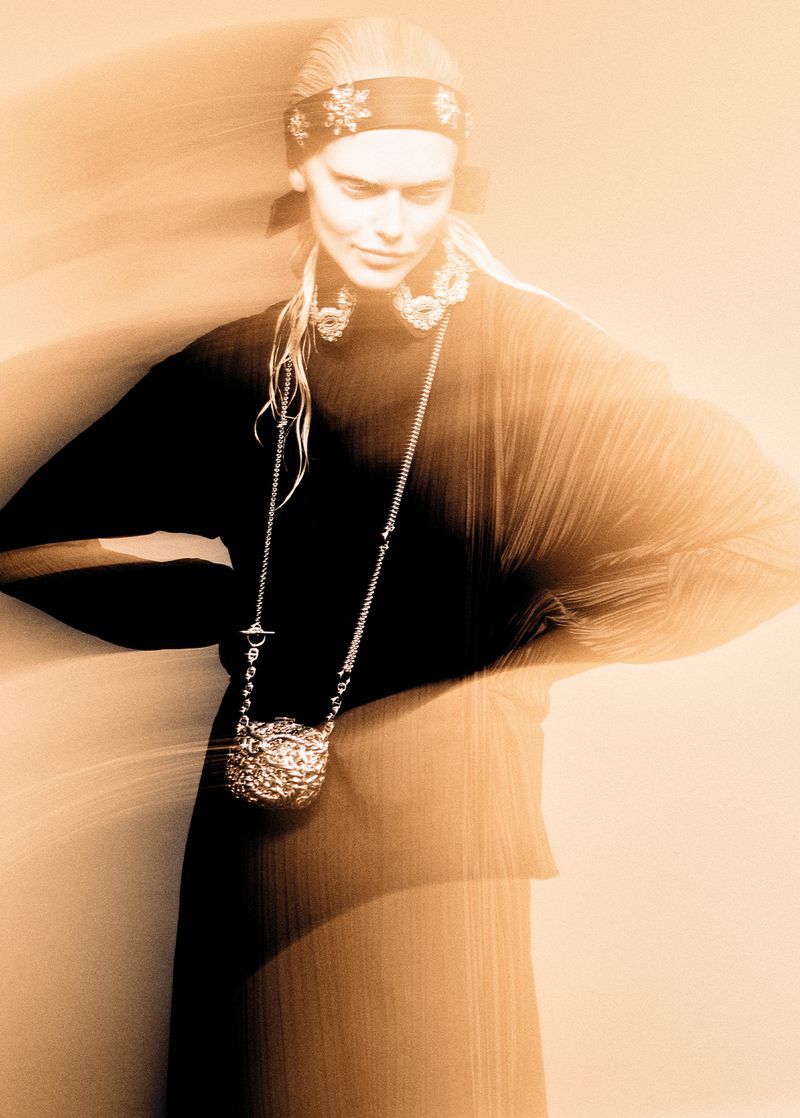 Fashion shot featuring an adult female model with a decorative headband, statement jewelry, and a handbag, set against a warm toned background.