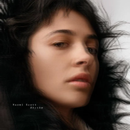 Portrait of a woman with dark wavy hair and tan skin with soft lighting, facing the camera in a close-up shot. Image has a dreamy aesthetic.