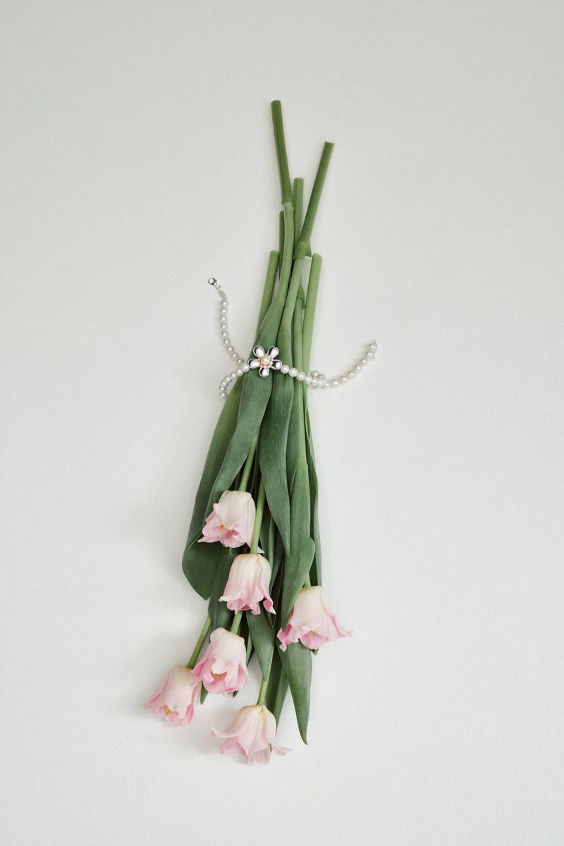 Bouquet of pink tulips tied with pearl necklace on a white background. Floral arrangement with elegant jewelry and spring flowers.